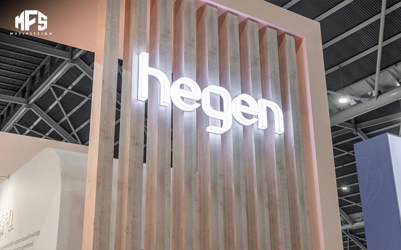 A brightly lit hegen logo is mounted on a wooden slatted display wall.