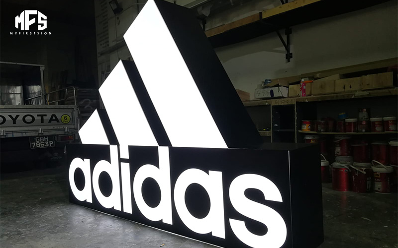 A large, free-standing illuminated Adidas logo and wordmark on a workshop floor.